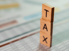 12 Tax Strategies for Small Business Owners in 2026 Vertical stack of wooden letter blocks spelling TAX against a blurred document background.