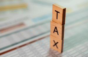 12 Tax Strategies for Small Business Owners in 2026 Vertical stack of wooden letter blocks spelling TAX against a blurred document background.