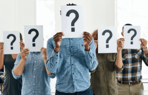 Business Valuation in 2026: How to Know What Your Company Is Worth Group of people in a bright office holding white signs with large question marks, obscuring their faces for anonymity or uncertainty.