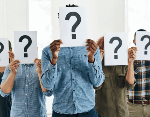 Business Valuation in 2026: How to Know What Your Company Is Worth Group of people in a bright office holding white signs with large question marks, obscuring their faces for anonymity or uncertainty.