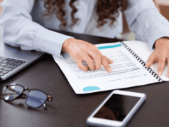 CPA vs Enrolled Agent in 2026: Which Tax Professional Do You Need? Person points to a financial report in a spiral notebook on a desk, with a laptop nearby.