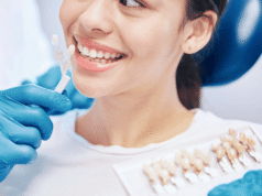 Dental Practice Tax Planning 2026: The Complete CPA Guide for Dentists Dentist in blue gloves holds tooth shade guide next to patient's smile to match tooth color.