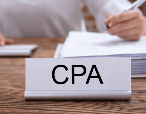 How AI Is Changing the CPA Industry in 2026 Close-up of a CPA nameplate on a desk with a stack of papers and a person writing in the background.