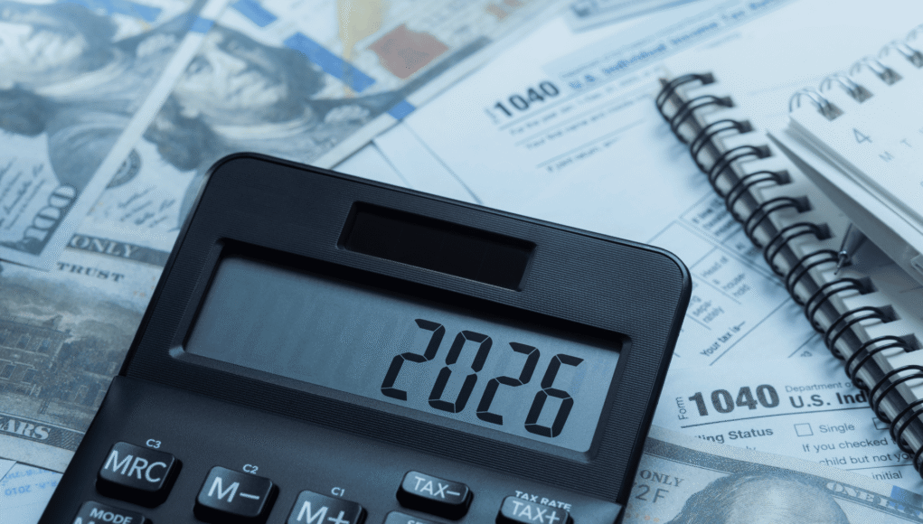 Close-up of a calculator on top of tax forms and scattered US dollar bills, with a spiral notebook nearby, suggesting accounting or budgeting.