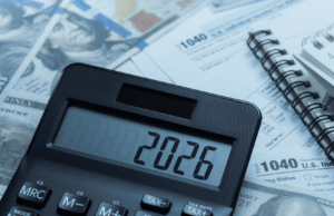 How to Buy a Dental Practice in 2026: Financial & Tax Guide for Dentists Close-up of a calculator on top of tax forms and scattered US dollar bills, with a spiral notebook nearby, suggesting accounting or budgeting.