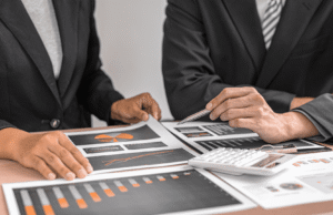 IRS Cryptocurrency Tax Rules 2026: What Investors Must Report Two professionals in suits review financial charts and graphs spread across a desk, using a pen and calculator nearby.
