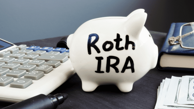Roth Conversion Strategy 2026: How High-Income Earners Can Save on Taxes White piggy bank labeled Roth IRA on a desk next to a calculator, pen, wallet, and stacks of cash—conveys retirement savings.