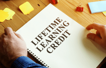 S-Corp vs LLC in 2026: Which Business Structure Saves You More Taxes? Notebook open to a page titled 'Lifelong Learning Credit' with hands resting on the page and yellow sticky notes on a wooden desk.