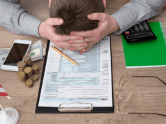 CPA Services for High Net Worth Individuals in 2026: Tax Planning & Wealth Person rests head in hands over a tax form on a clipboard, surrounded by money, phone, and calculator in a stressful office scene commonly linked to finances.